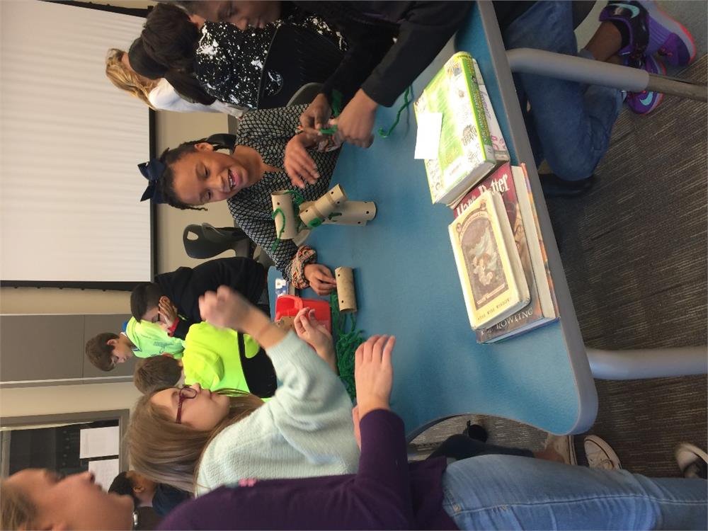 A group of students seated at a table, with their hands placed on the surface, engaged in discussion or collaboration.