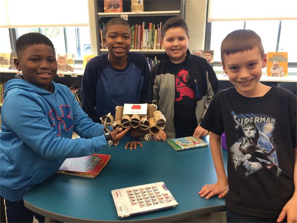 Four boys smiling and posing together, holding a book in their hands for a group photo.