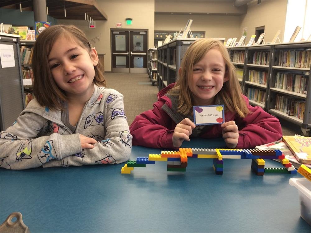 Two girls engaged in play, sitting at a table surrounded by colorful Lego bricks, showcasing creativity and collaboration.