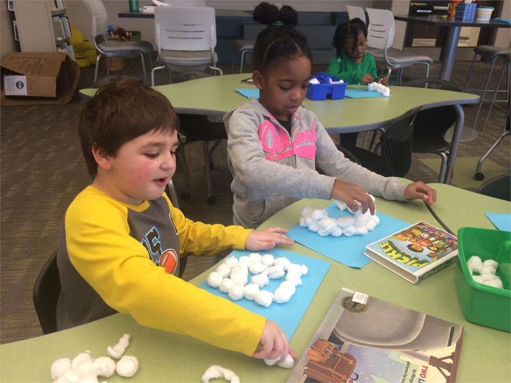 Two children joyfully create snowballs together at a table, surrounded by a winter wonderland.