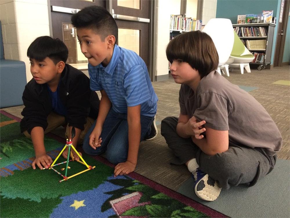 Three boys engaged in play with a model of a pyramid, showcasing creativity and teamwork in their activity.
