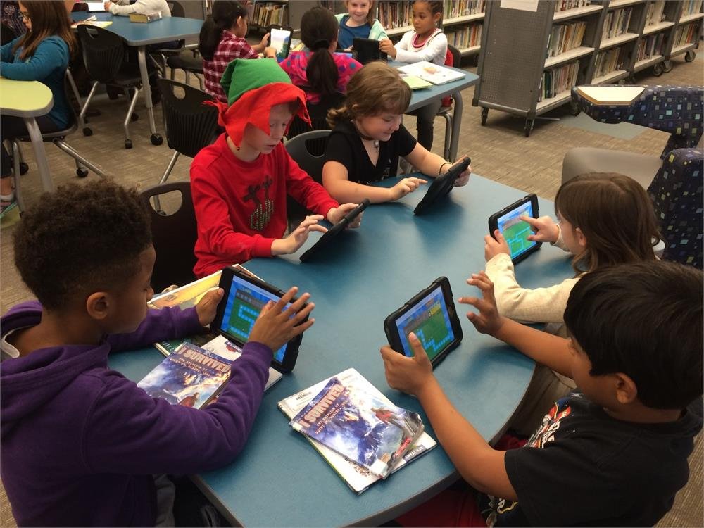 Children engaged with tablets while seated at tables in a library, exploring digital resources and learning materials.