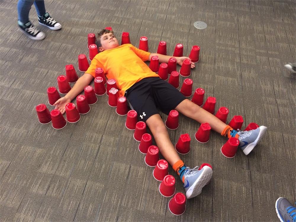 A boy lies on the floor, surrounded by scattered red cups, creating a playful and vibrant scene.