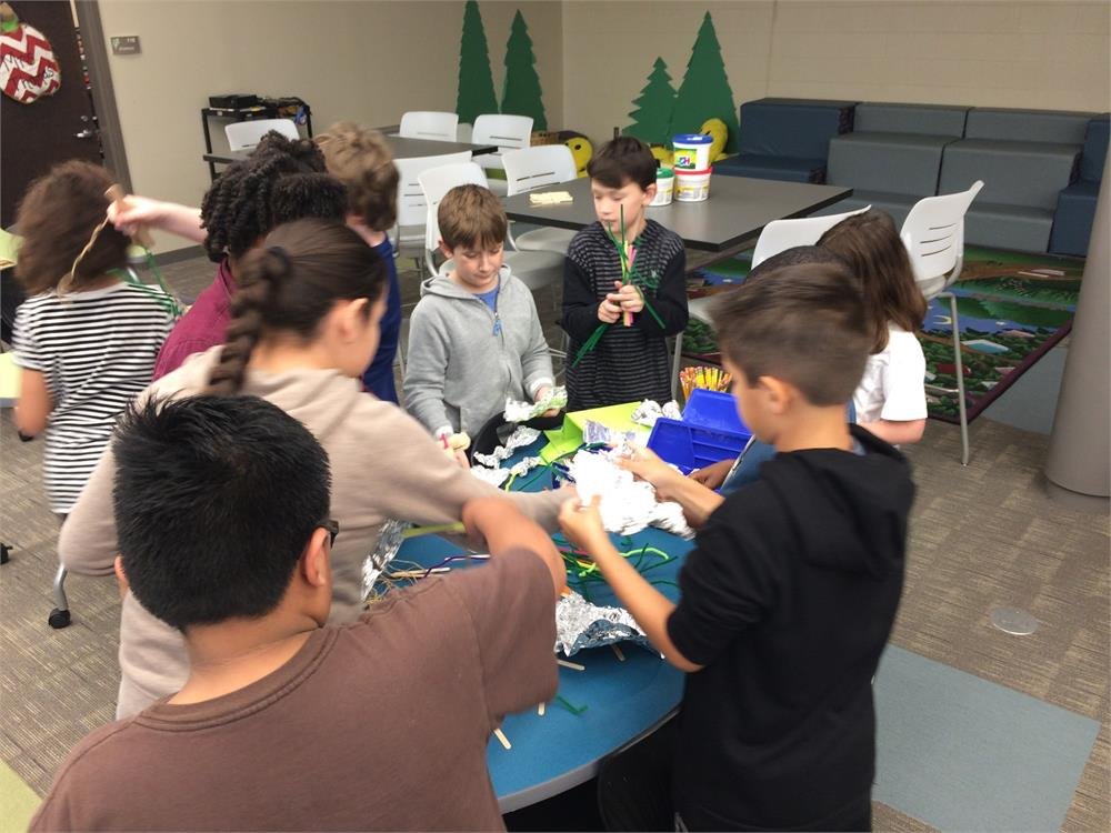 Students collaborate on a project in the library, surrounded by books and study materials, focused on their work.