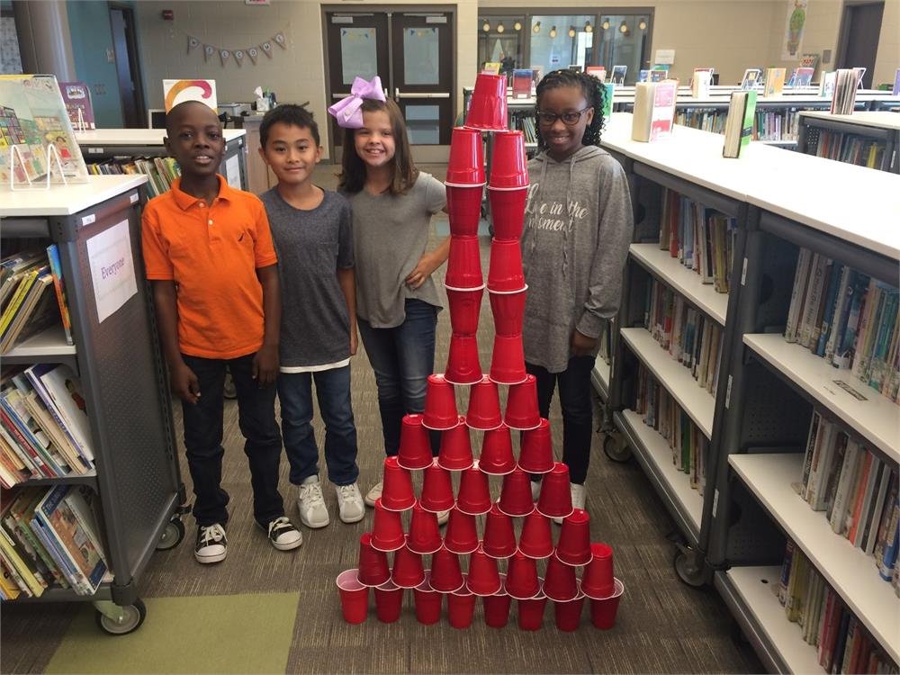 Students in a library collaborating to construct a tower using plastic cups, showcasing teamwork and creativity.