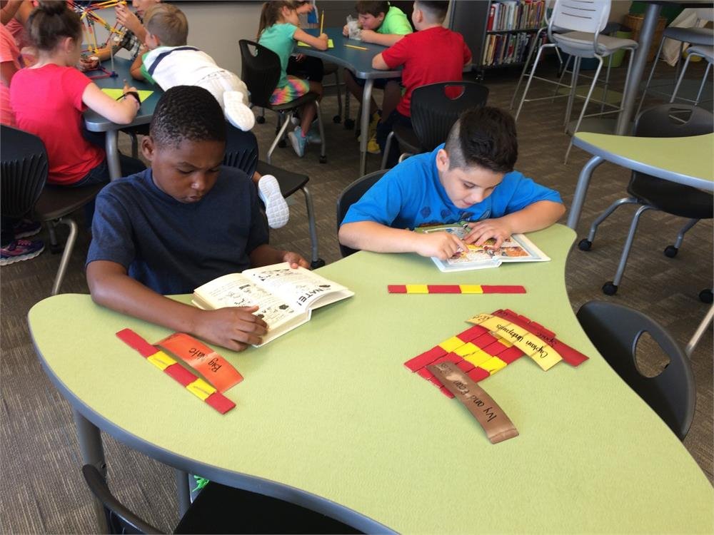 Two boys collaborate on a colorful puzzle at a table, focused on fitting the pieces together.