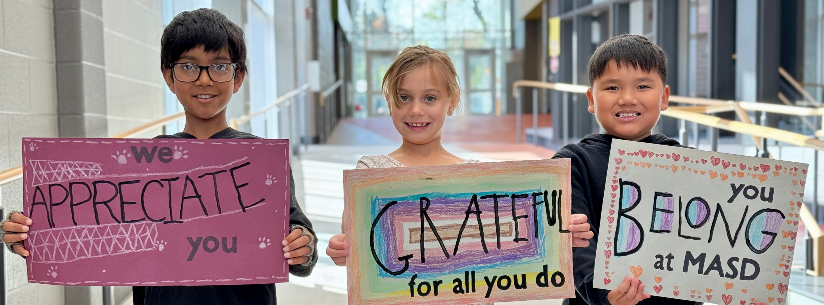 Three students holding signs that send a message of appreciation and belonging within our school community.