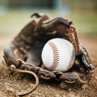 Bentley Athletics - Photo of a baseball and glove on the ground.