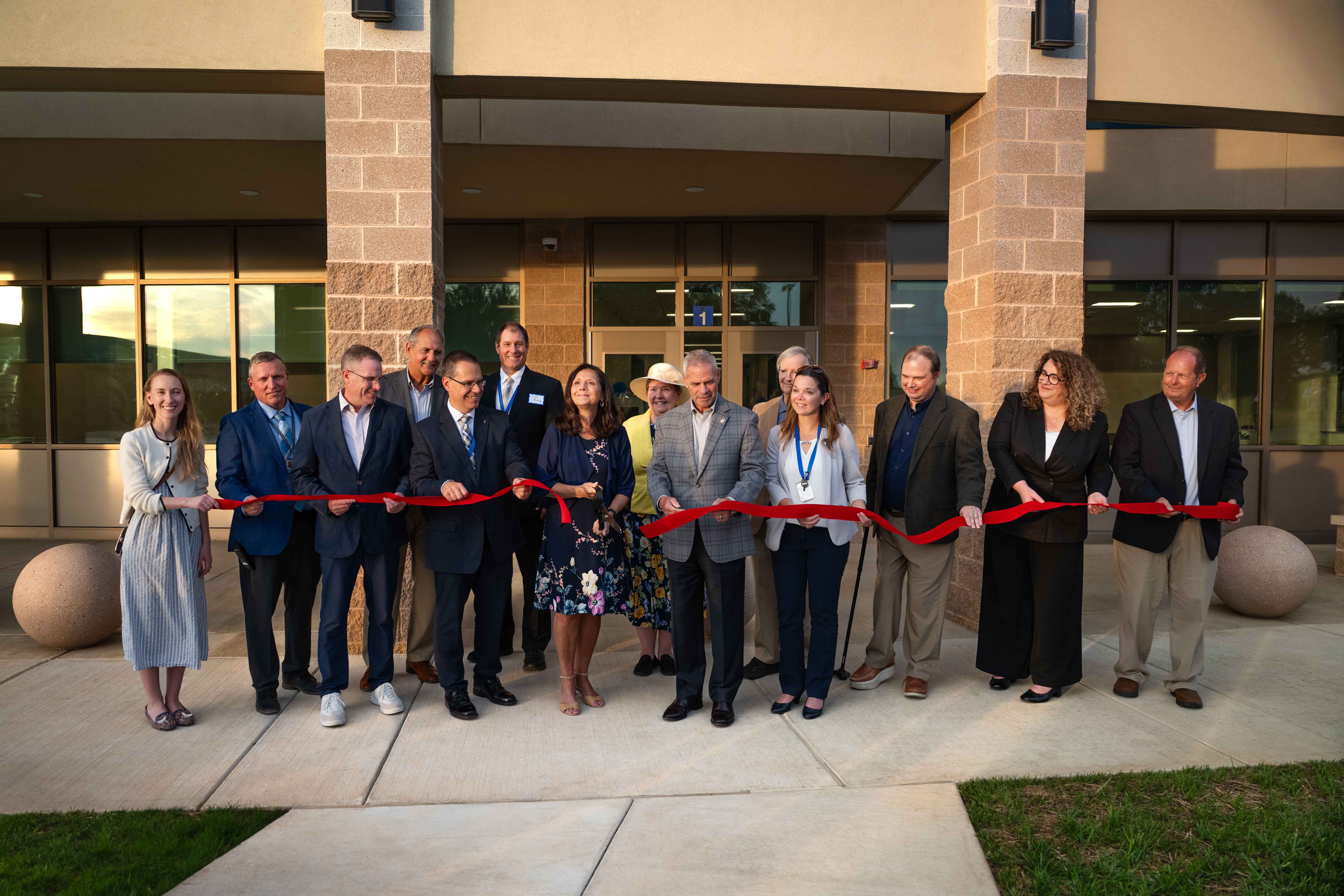 group of people in a line cutting a large ribbon with oversized scissors to mark the official opening of a new building