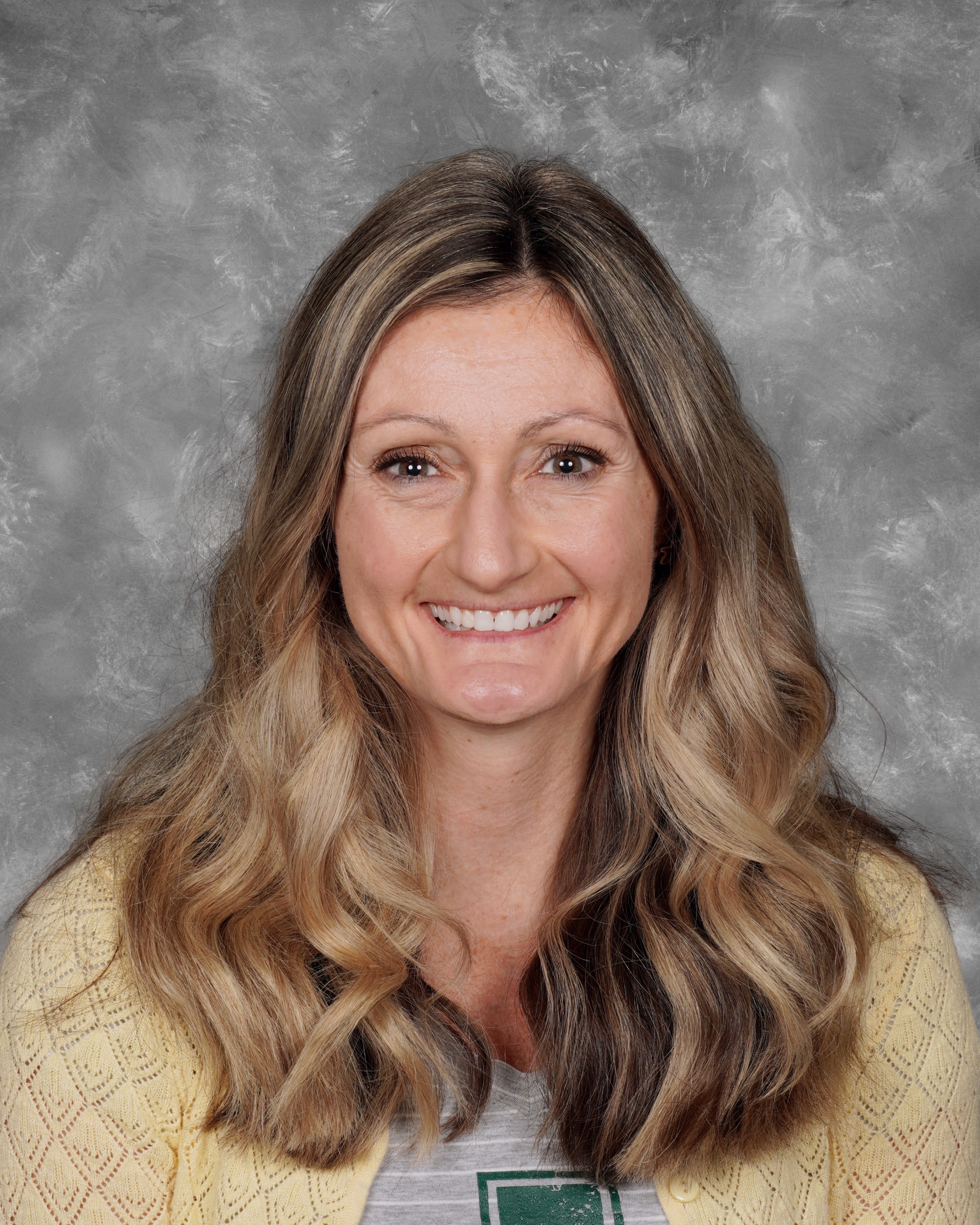 Erica Stallings school picture on a gray background. Erica is smiling, has long blonde hair with a yellow sweater and gray amherst t-shirt