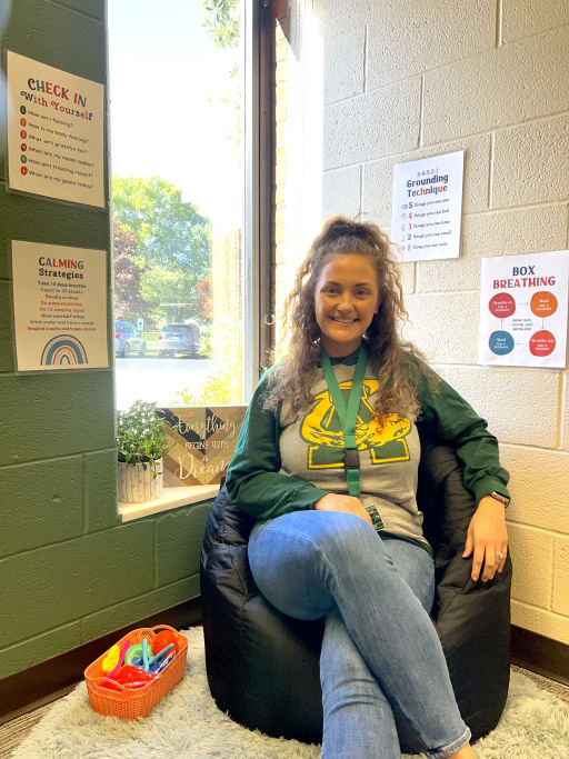 A person with curly hair sits comfortably in a bean bag chair in a brightly lit room, surrounded by posters on the walls and a window showing greenery outside.