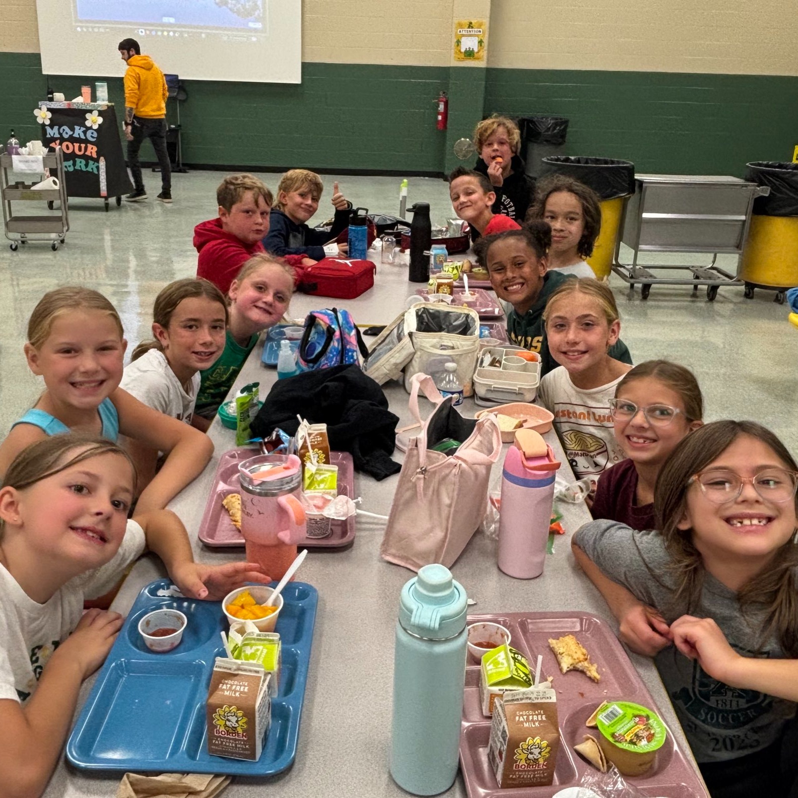 Students smiling for a picture in the lunch room as they eat lunch