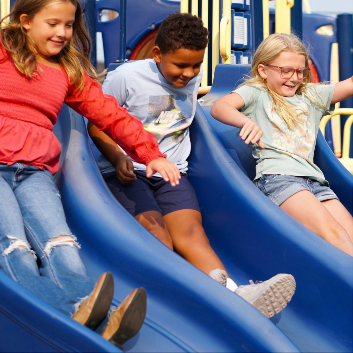three belle elementary students going down a triple slide on the playground.