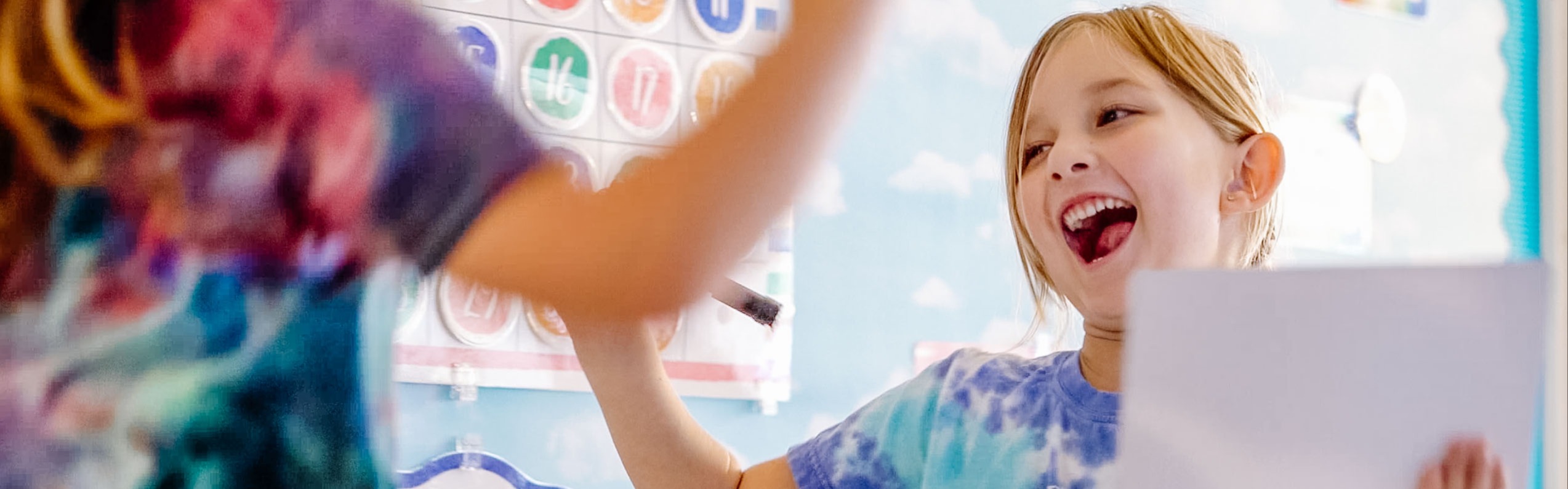 kindergarten student smiling after writing down the correct answer during a classroom lesson.