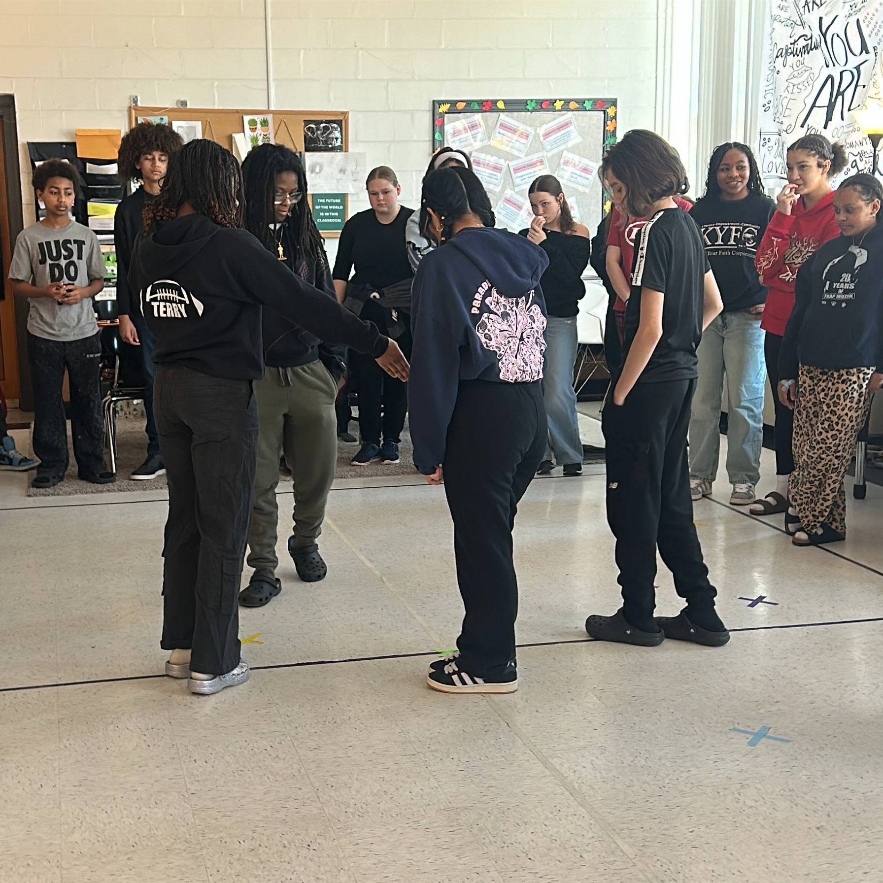 A life size graph has been made out of tape on the floor of a classroom. Students are standing at different spots on the graph. The students are acting as data points on the graph as part of a math lesson.