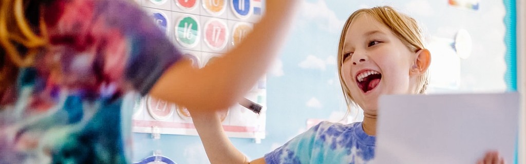 kindergarten student smiling after writing down the correct answer during a classroom lesson.
