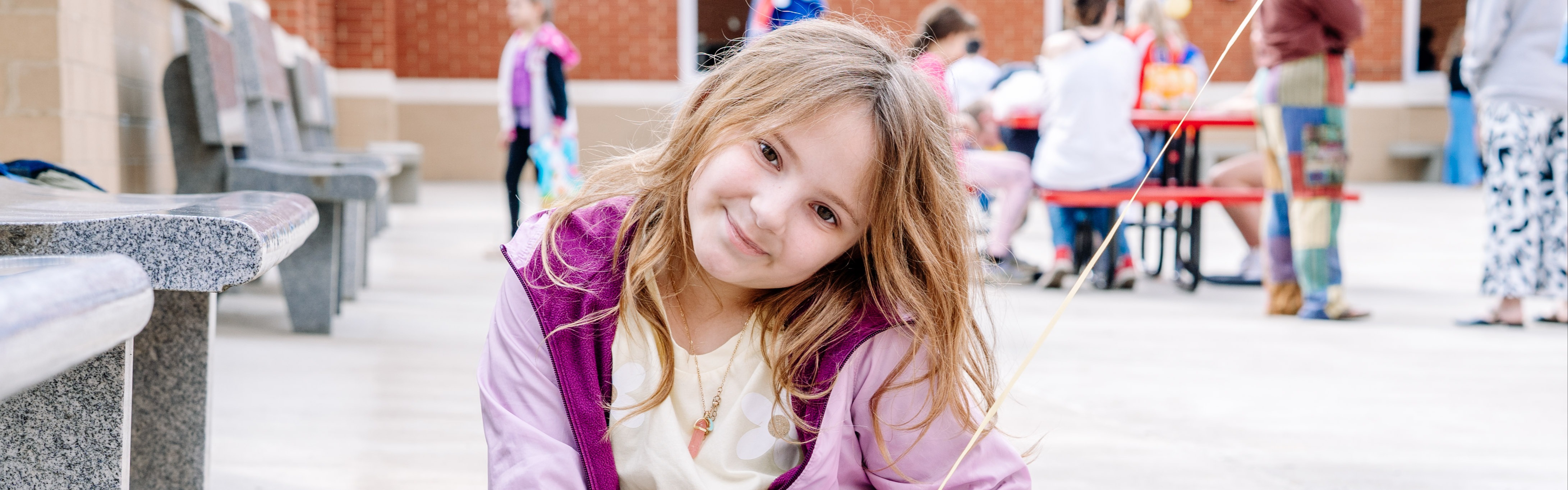 A young student is sitting down on the ground and smiling for a picture.