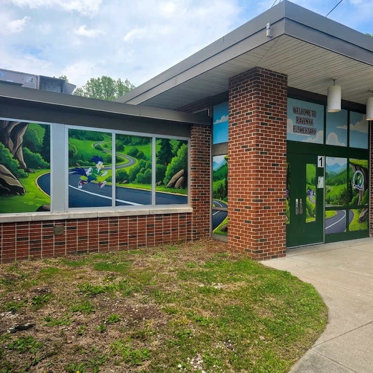 The front entrance of Ruffner Elementary School. The windows are covered in a perforated vinyl wrap. The theme for the wrap is based on the school's mascot, the road runners. On the window to the left of the front door, Ruffner Roadrunner is running on a road that is winding through the mountains. 