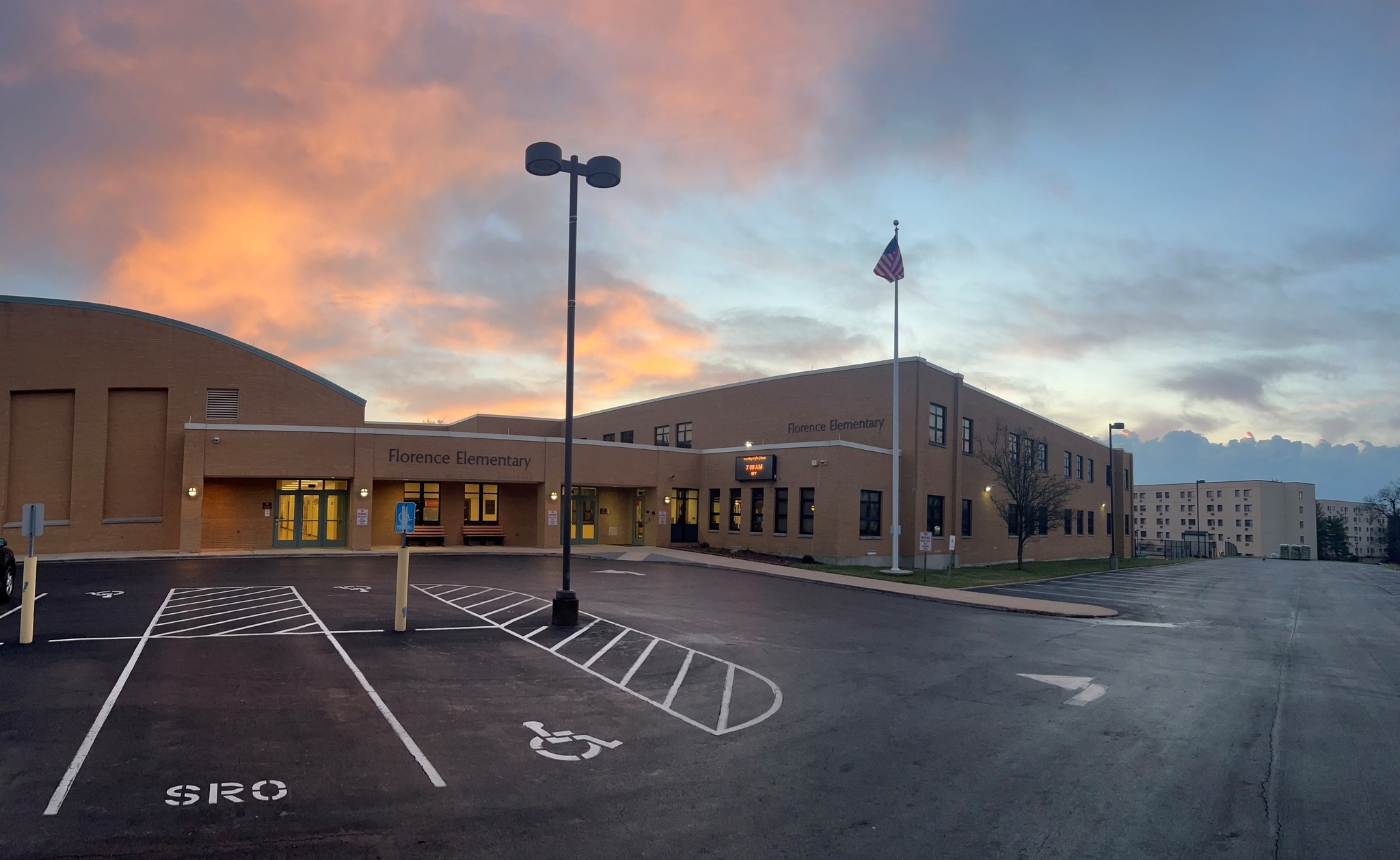 Large building with flagpole and empty parking lot. Pink and blue sky. Accessible parking spot.