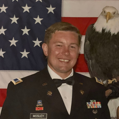 Justin Moseley stands in his uniform in front of the American Flag and a painting of an eagle.