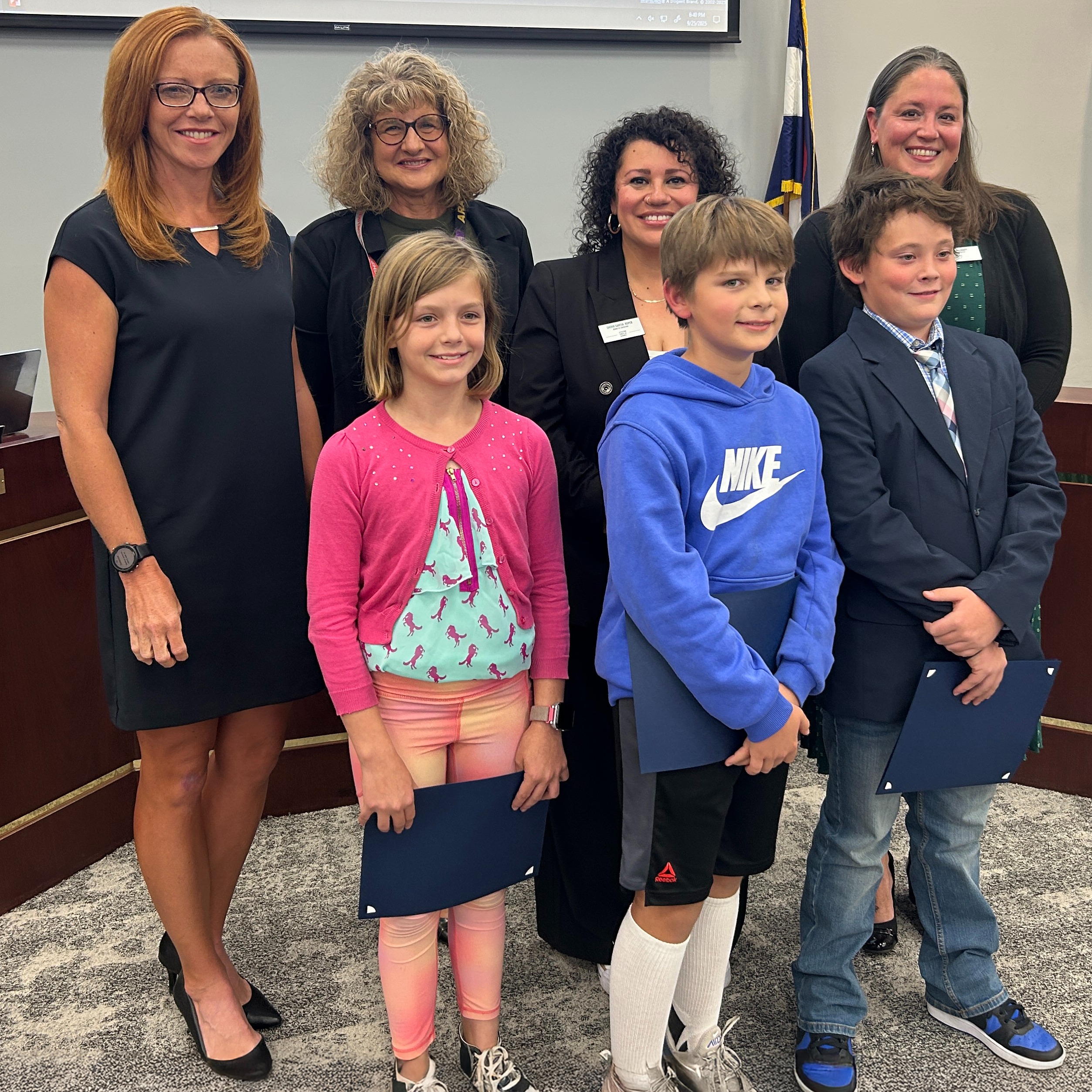 Three students hold their Student Spotlight certificates and stand with Board members in the LPS Boardroom.
