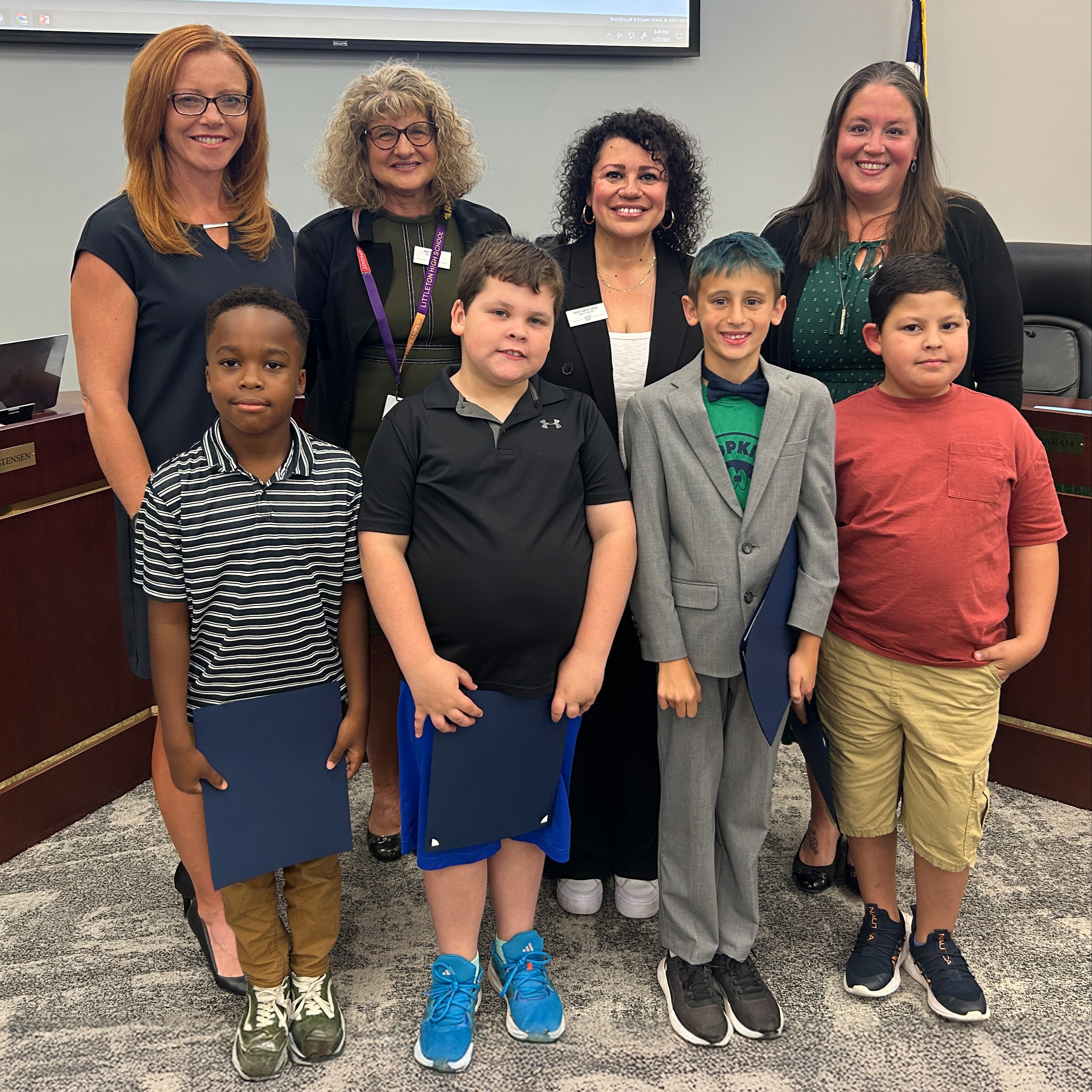 Four students hold their Student Spotlight certificates and stand with Board members in the LPS Boardroom.
