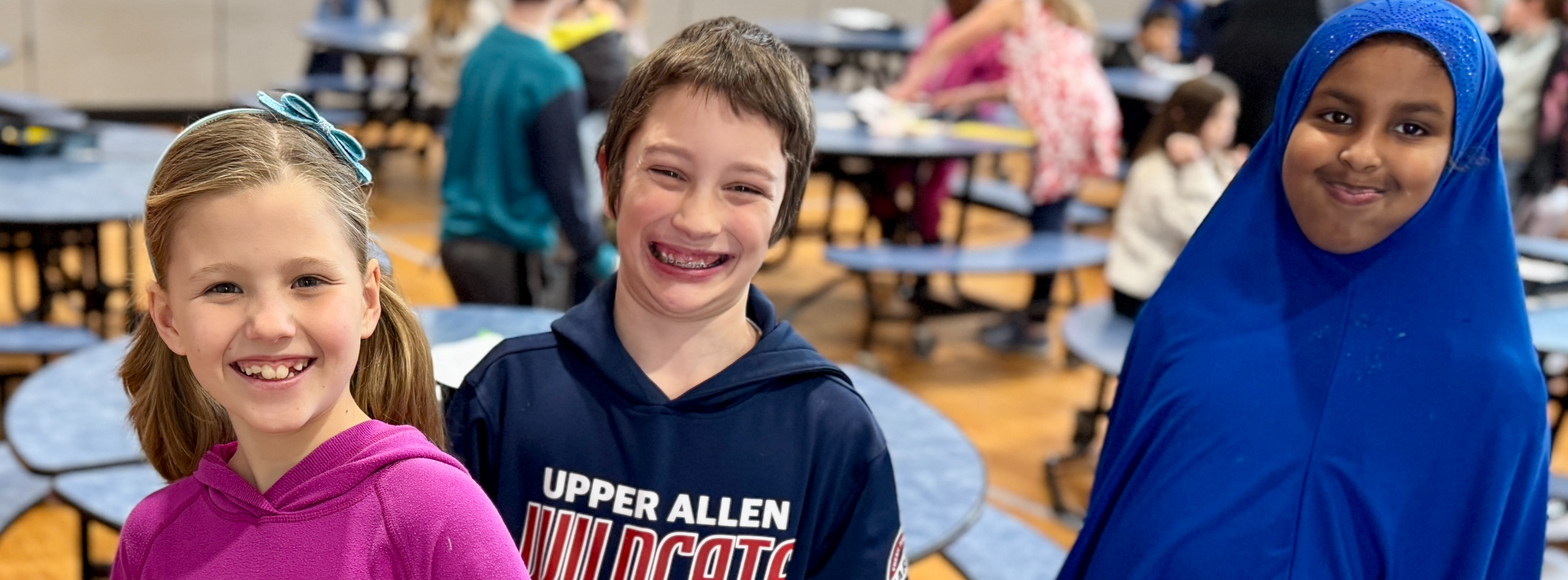 Three young students standing together in the cafeteria, all smiles.