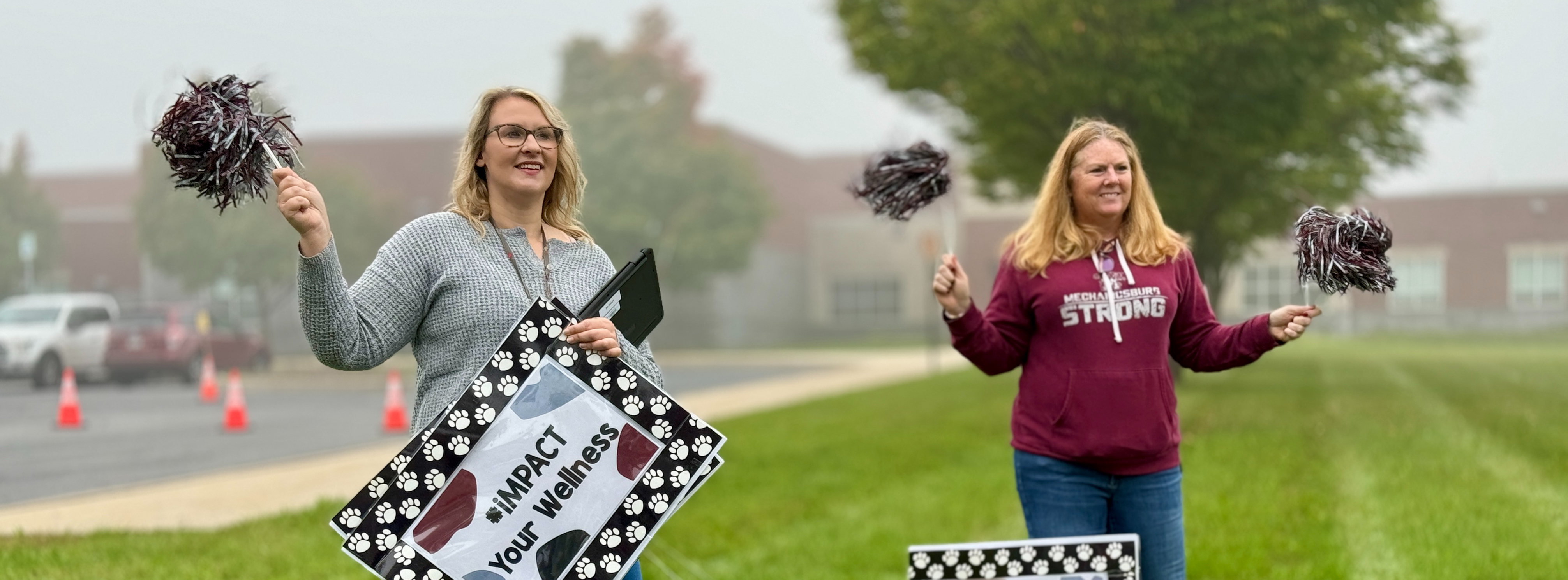 Two teachers holding pom poms and wellness signs.