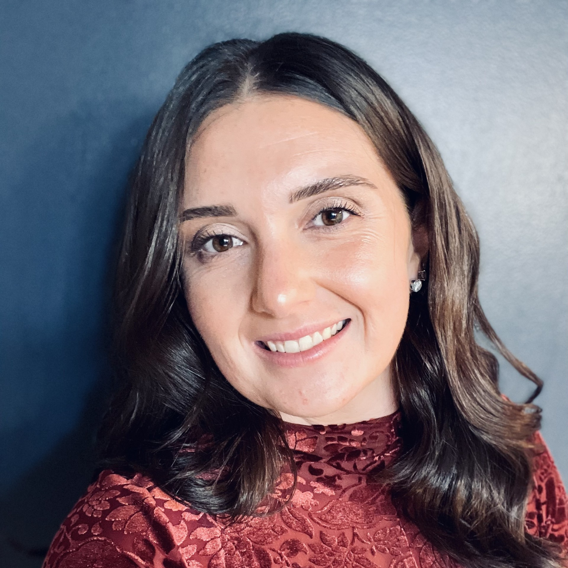A woman with long, brown hair smiles at the camera against a blue background.