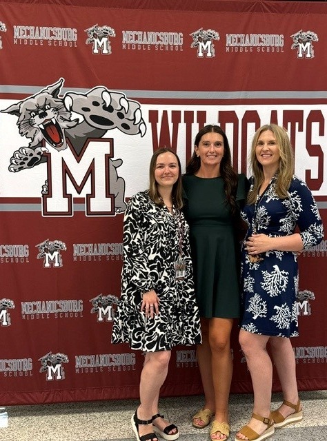 Three women stand in front of a Mechanicsburg MIddle School Wildcats backdrop.