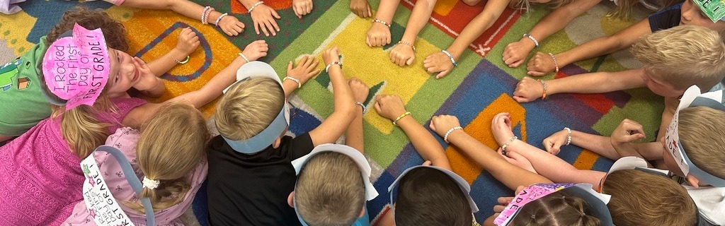 1st grade students putting hands in together while laying on a letter rug