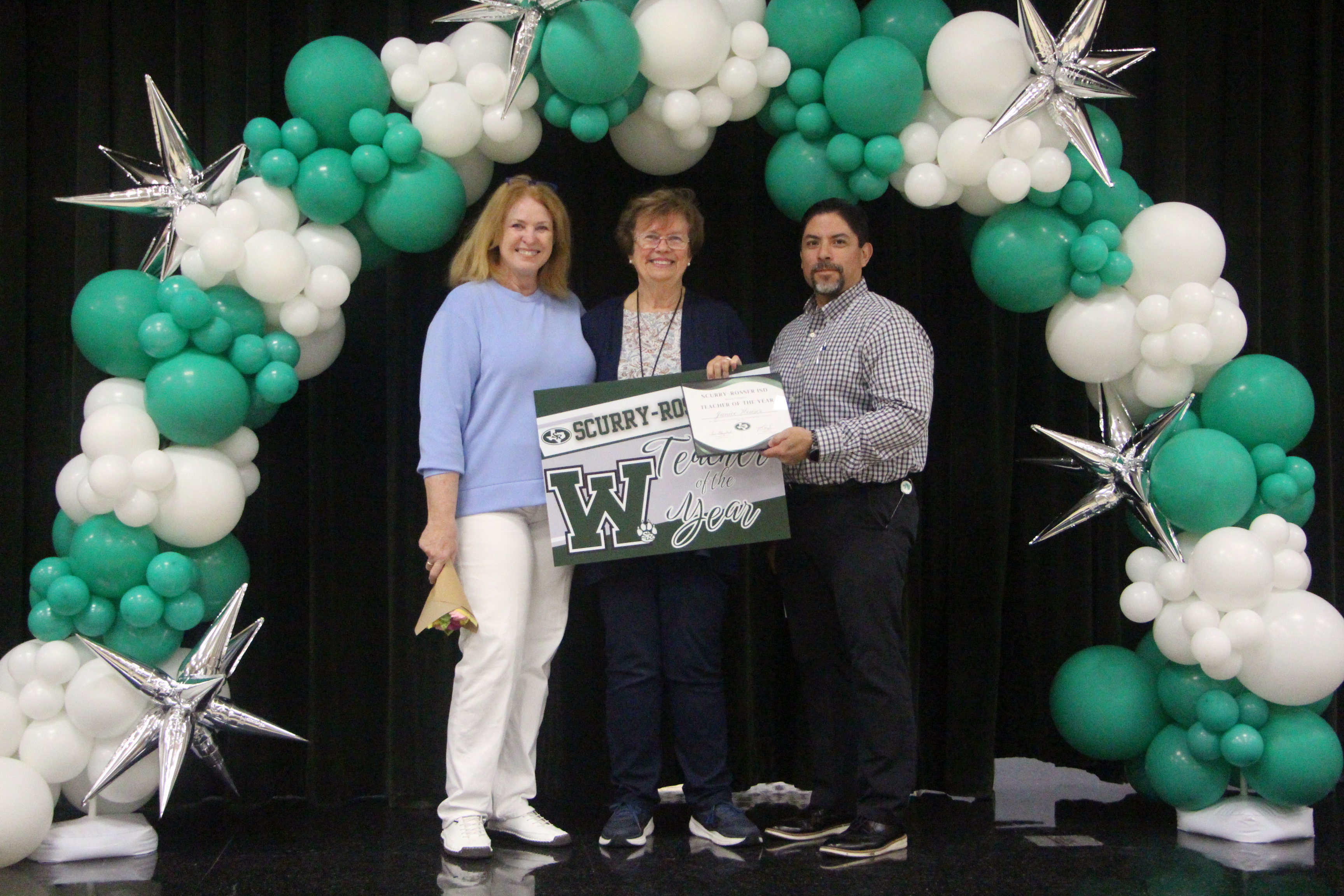 two women and one man stading under a green and white balloon arch