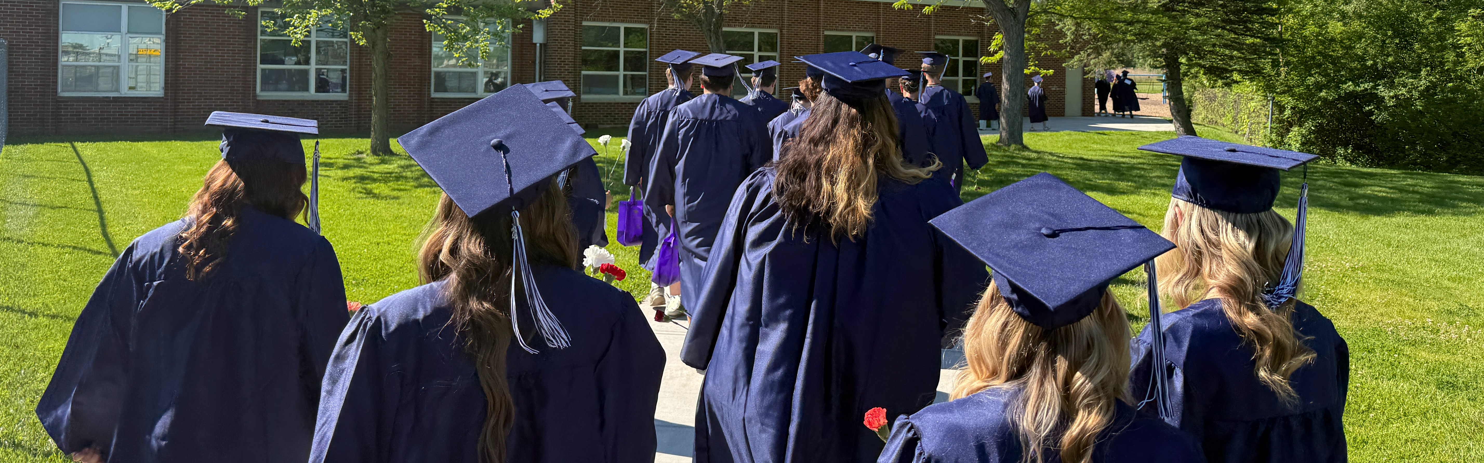 students in caps and gowns walking towards the elementary school