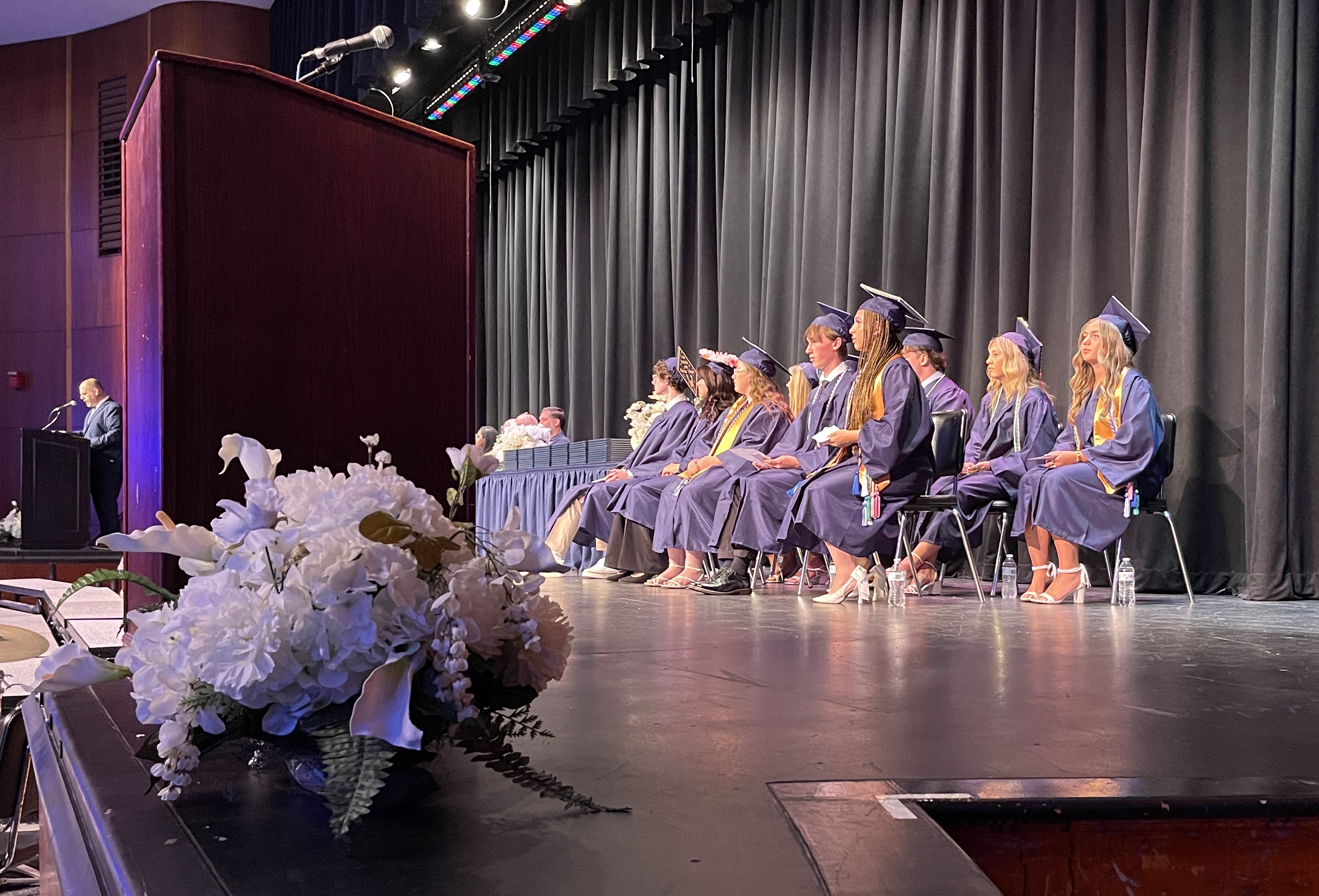 class officers and top of class students sitting on stage at graduation in caps and gowns