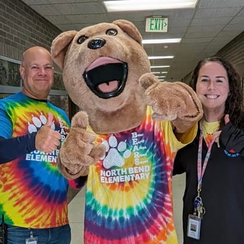 Principal Greg Lane, Assistant Principal Megan Donnelly, and the School Mascot Bendy Bear standing together giving a thumbs up.