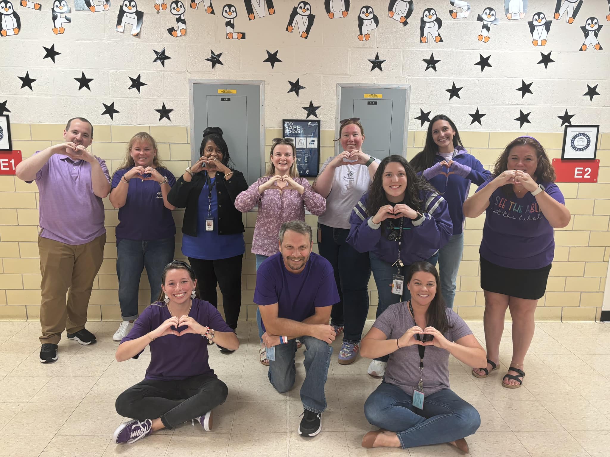 Picture of a group of adults smiling at camera and making a heart with their hands.