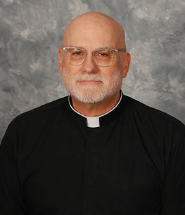A middle-aged man with glasses and a bald head, wearing a black clerical shirt with a white collar, poses against a gray backdrop.