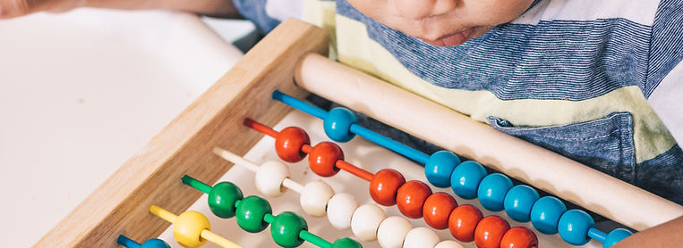 A young child is playing with a colorful wooden abacus, focusing on the beads while seated at a table.