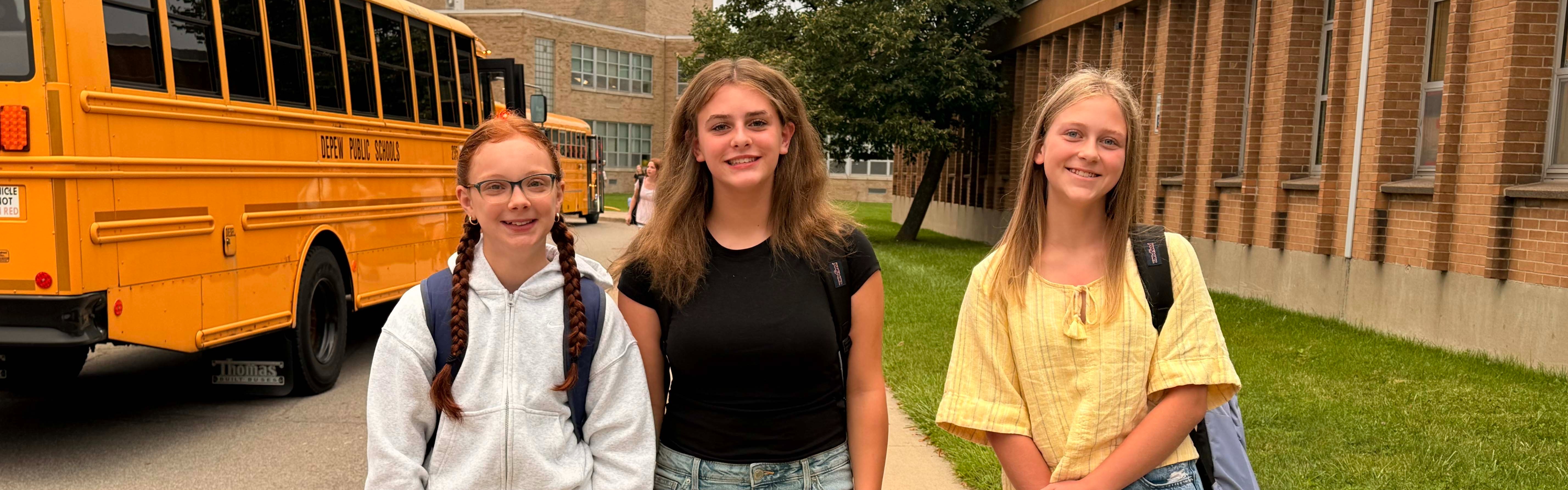students smile as they arrive on first day with bus in background