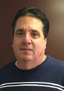 Person wearing a navy blue sweater with white stripes, standing against a brown background. The focus is on their upper body.