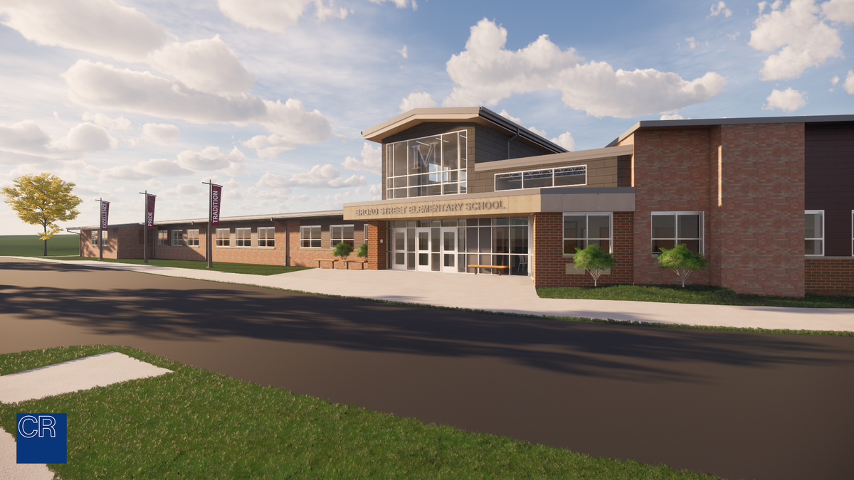 A modern school building featuring a large glass entrance, brick exterior, and landscaped surroundings under a partly cloudy sky.