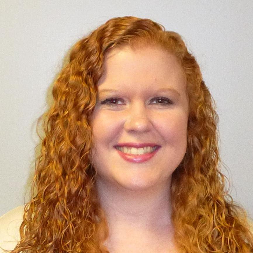 A woman with long, curly red hair smiles at the camera against a plain background.