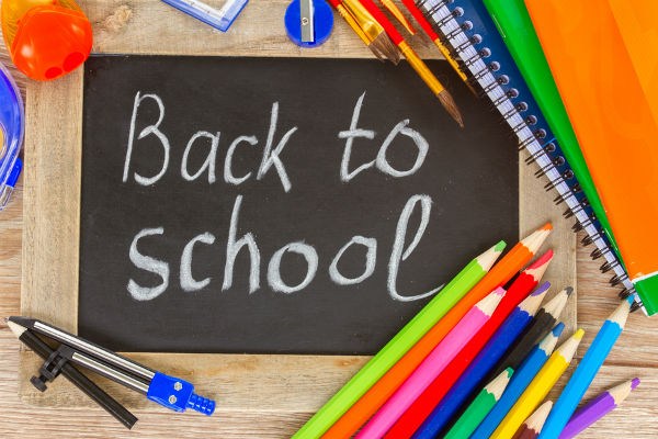 A chalkboard with the words 'Back to school' written in white chalk, surrounded by colorful school supplies including pencils, markers, and notebooks.