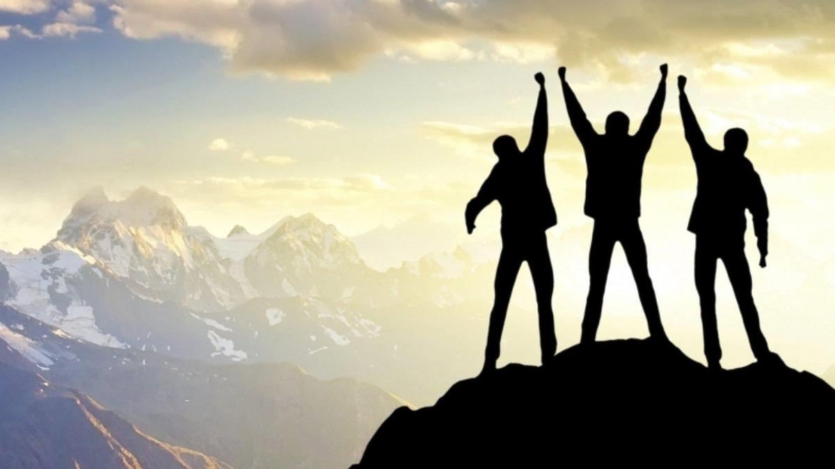 Three silhouetted figures stand triumphantly on a mountain peak, raising their arms against a backdrop of a scenic sky and distant mountains.