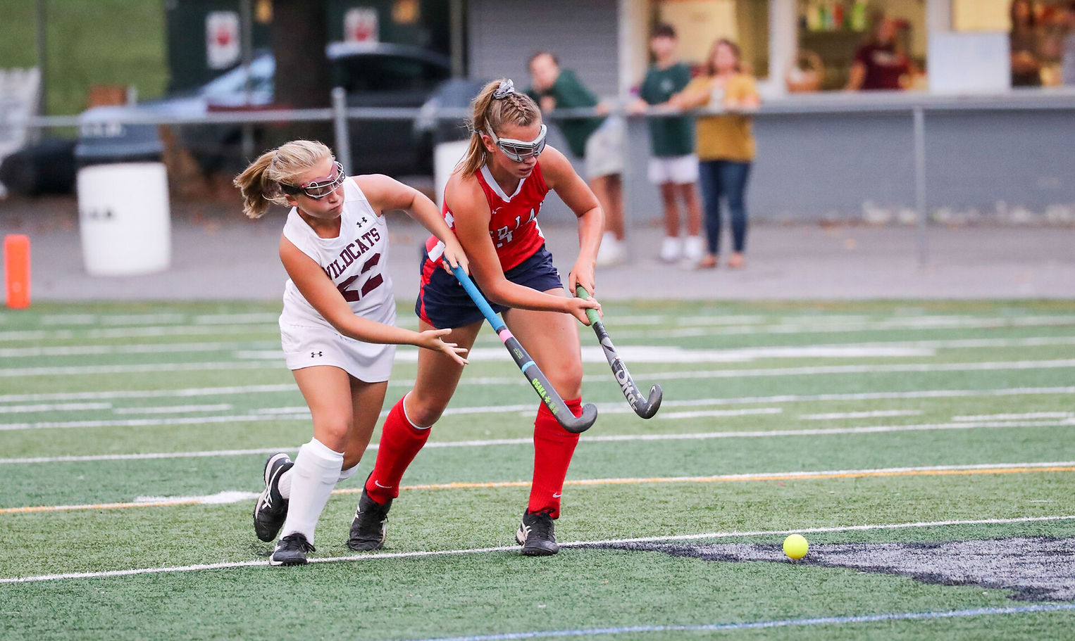Two female field hockey players compete for control of the ball on a turf field during a match.