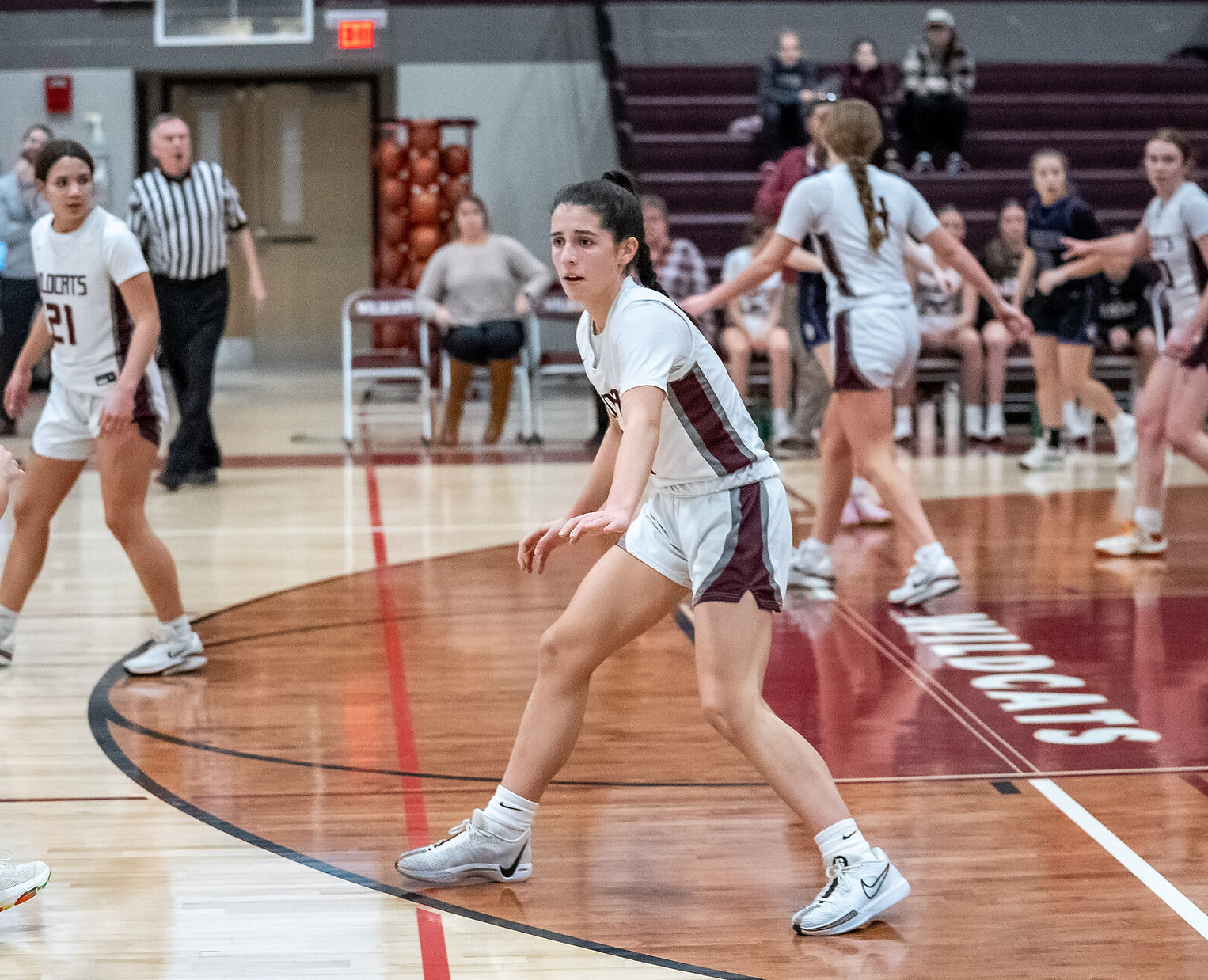 A female basketball player is poised on the court, ready to receive the ball, while teammates and opponents are positioned in the background during a game.
