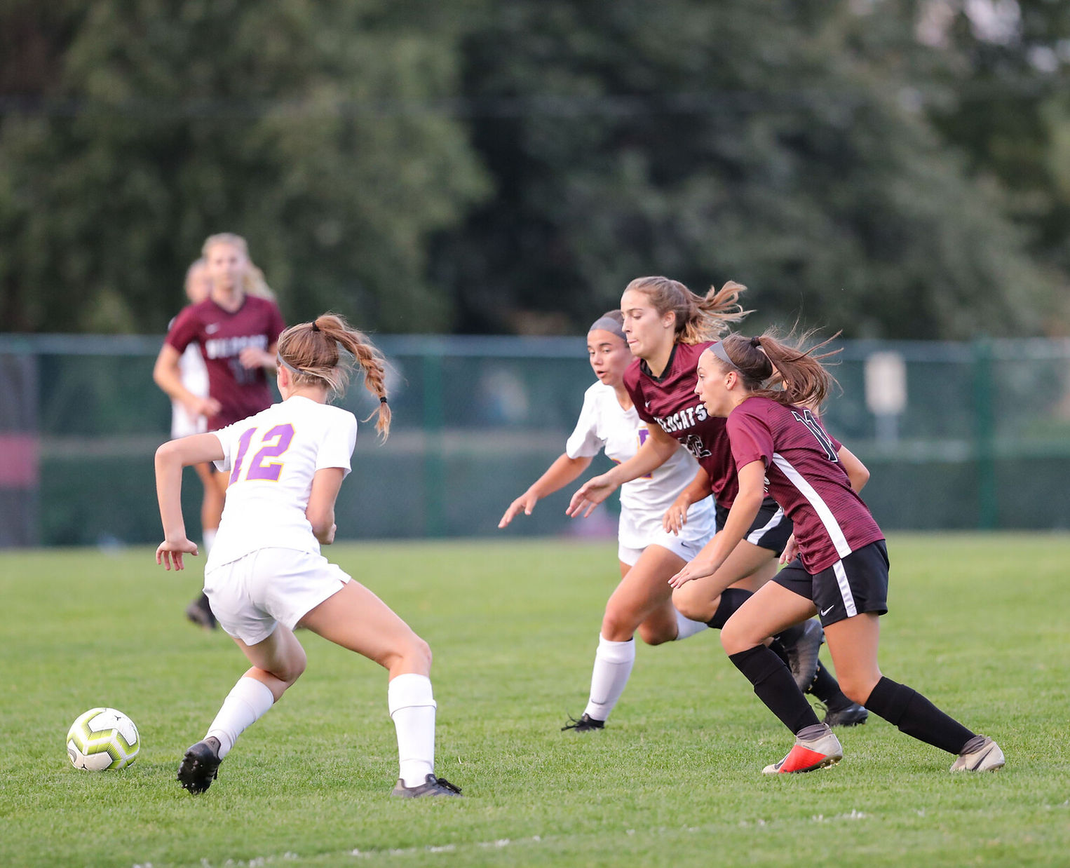 A dynamic soccer match in progress, featuring players in white and maroon uniforms competing for the ball on a grassy field.