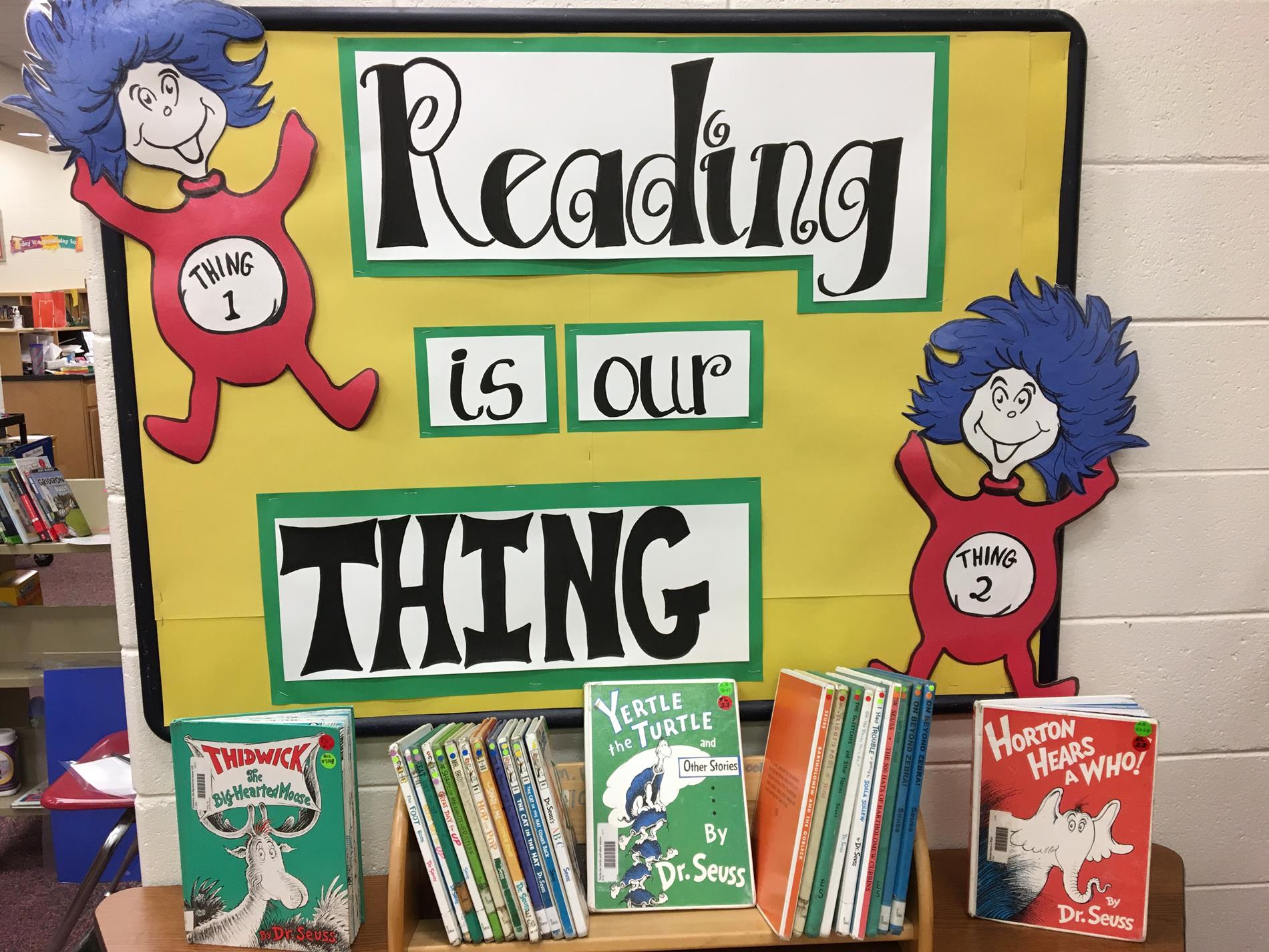 A colorful display promoting reading, featuring the phrase 'Reading is our THING' with cartoon characters on either side and a selection of Dr. Seuss books arranged at the bottom.