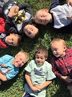 A group of kids all laying down on the grass and smiling at the camera