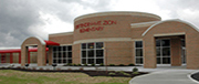 A modern brick building with large windows and a rounded entrance, featuring the name 'International Academy' prominently displayed above the entrance.
